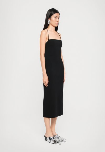 Black midi dress with thin straps, fitted silhouette, and smooth texture. Paired with metallic, open-toe heeled mules and statement earrings.