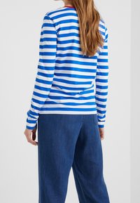 Blå och vit randig skjorta med lång ärm och rund halsringning, kombinerad med löst sittande blå denimbyxor som ger en avslappnad passform och slät textur.