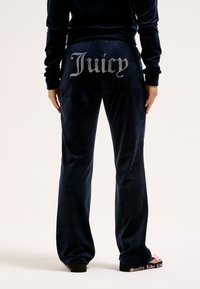 Jūras spēku velūra sporta bikses ar "Juicy" logo ar rhinestones aizmugurē. Iezīmējumam ir ērta vidukļa daļa un taisna kāju forma.