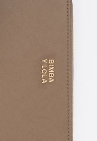 Hnedá textilná taštička s pozláteným embosovaným logom "BIMBA Y LOLA". Vyznačuje sa čistými líniami a jemne prešitým okrajom. Hladká textura.