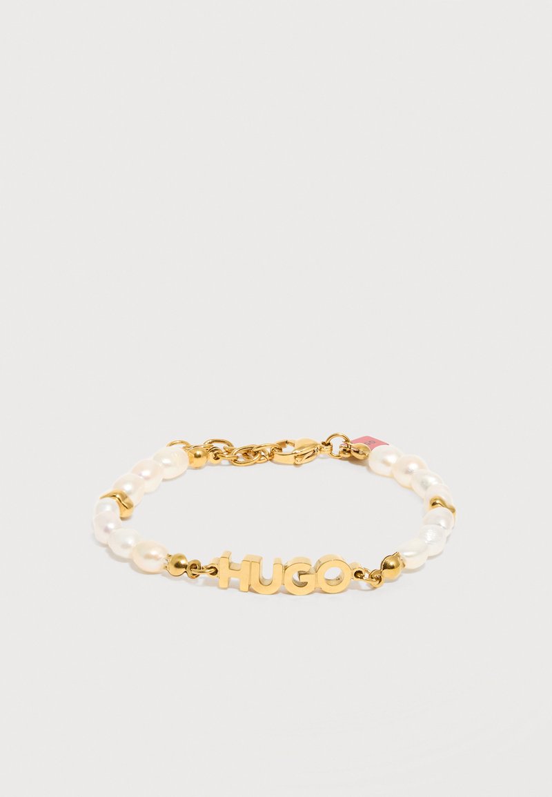 Βραχιόλι από χρυσό και μαργαριτάρι με κούμπωμα αστακού, με χρυσά γράμματα που σχηματίζουν τη λέξη "HUGO" στο κέντρο.