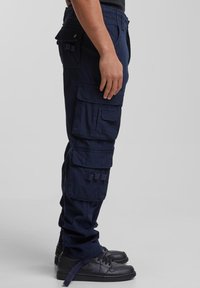 Marinblå cargobyxor med flera fickor, har en avslappnad passform, mjuk textur och justerbara detaljer i metall för praktisk användning.