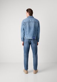 Denim jacket and pants in light blue. Jacket features a classic collar, and rear pocket label. Pants are straight-leg with subtle fading.