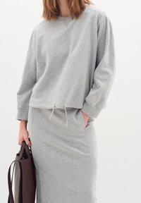 Sudadera gris de corte holgado, con cordón en el dobladillo, mangas largas y puños acanalados. Combina con una falda gris a juego.