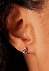 Silberne ohrringe in Blumenform mit einem runden Perlenakzent. Die Bl�ütenblätter aus glattem Metall und die geschwungenen Blätter sind vor einer strukturierten Haut angeordnet.