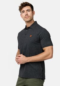 Polo shirt gris foncé avec un tissu texturé, patte de boutonnage à trois boutons et un petit logo orange sur la poitrine. Manches courtes et fentes sur les côtés.