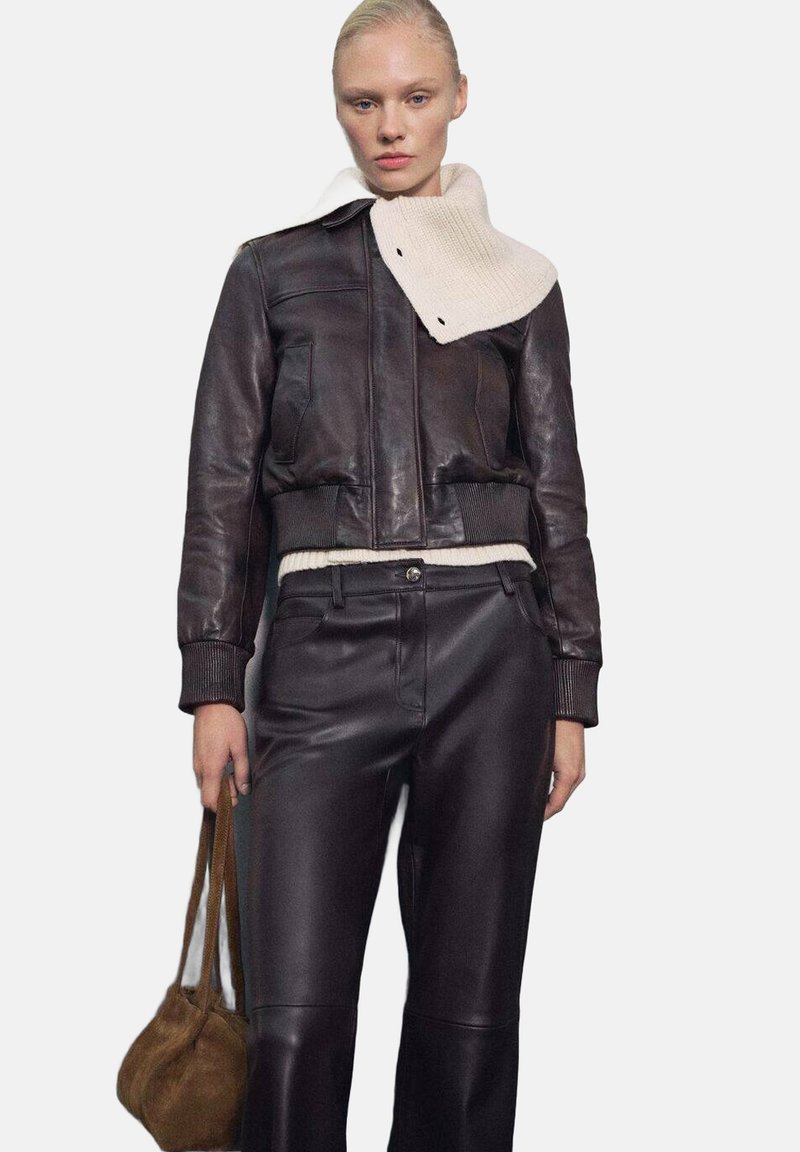 Bruine leren cropped jack met geribde manchetten, voorzien van een witte gebreide kraag. Gekleed met bijpassende bruin leren broeken en een kleine bruine tas.