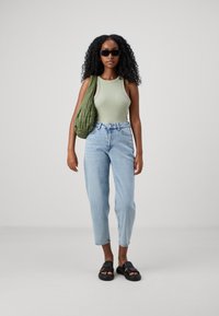 Grünes geripptes Tanktop, hellblaue hochgeschnittene Jeans, schwarze Plateausandalen und eine gesteppten olivgrüne Umhängetasche. Glatte Texturen und lässiger Stil.