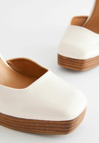Chaussures plateformes en cuir blanc avec un bout carré et une base en bois texturé. Finition lisse avec un design à côté ouvert.