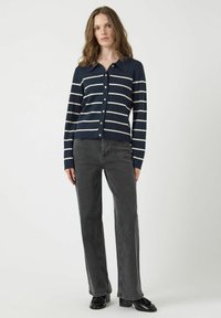 Marinblå ribbad cardigan med vita horisontella ränder, med krage och knappstängning, i kombination med grå raka jeans och svarta skor.