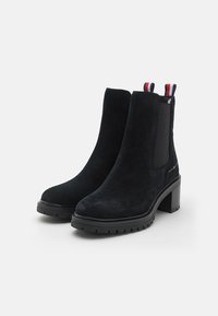 Bottines en daim noir avec un talon carré, des panneaux latéraux élastiques et des languettes à rayures. Surface texturée et semelle en caoutchouc épaisse.