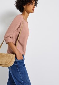 Top de manga larga de color rosa claro y textura, combinado con pantalones vaqueros anchos de color azul. Un bolso cruzado de ante beige reposa sobre la cadera.
