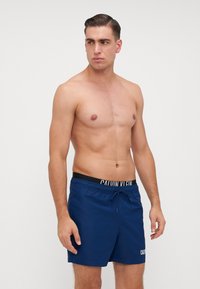Calções de banho azul marinho com cintura elástica, apresentando um logótipo branco. Feitos de um tecido suave, com cordão de ajuste para um encaixe personalizado.