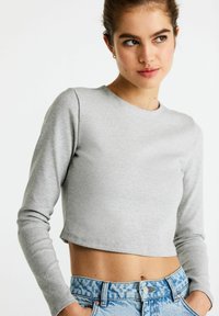 Sivý dlhý rukáv cropped top vyrobený z mäkkej látky, spárovaný s svetlomodrými vzorovanými vysokými džínsami. Jednoduchý a moderný dizajn.