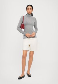 Light gray turtleneck sweater, white knee-length shorts, black ballet flats, and a small red handbag, worn with a neutral background.