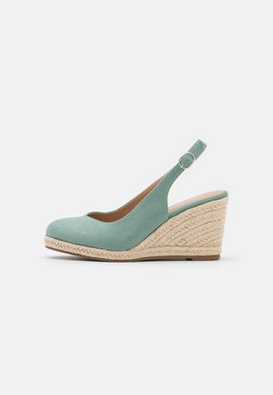 Chaussure compensée en daim vert clair avec design à bride arrière, détails complexes en jute tissé sur la semelle compensée, bout arrondi et petite boucle circulaire.