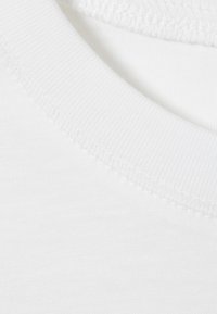 Gros plan sur l'encolure d'un t-shirt blanc en coton montrant la couture du col côtelé et la texture lisse du tissu.