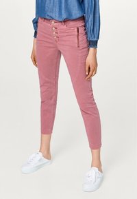 Jeans cropped attillati rosa con chiusura a cinque bottoni, zip laterali e tasche frontali. Abbinati a un top in denim e sneakers bianche.