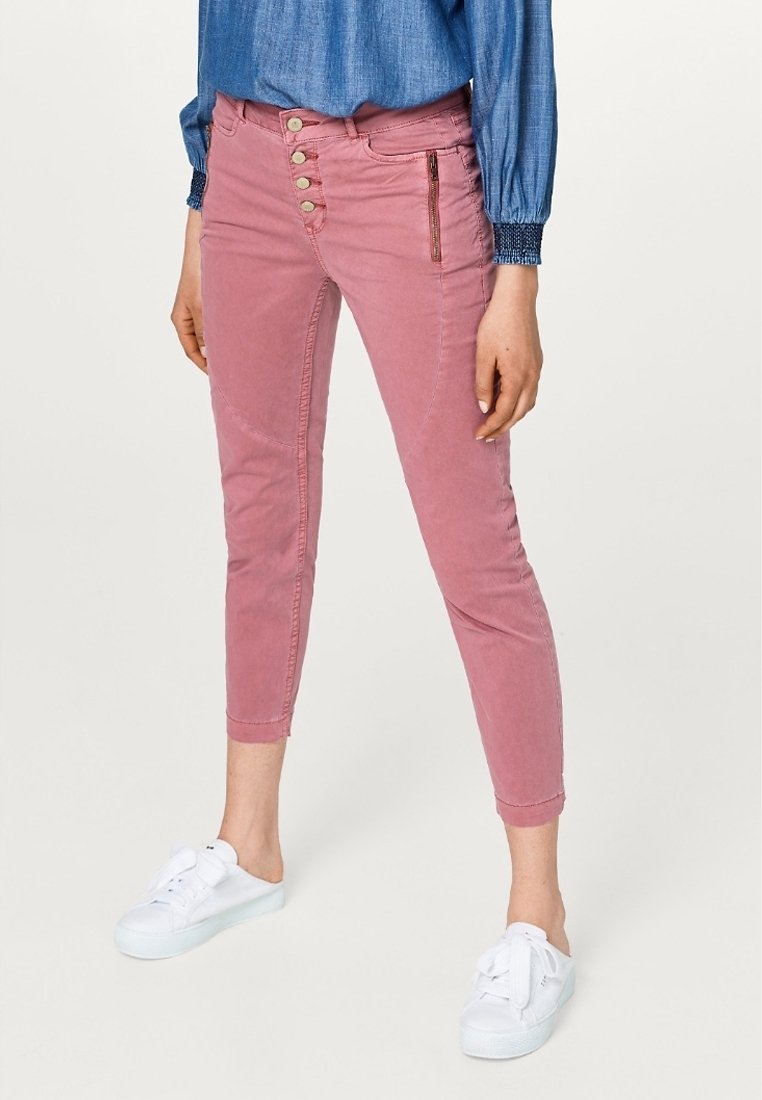 Jeans cropped attillati rosa con chiusura a cinque bottoni, zip laterali e tasche frontali. Abbinati a un top in denim e sneakers bianche.