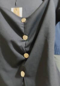 Svart stofftopp med V-halsdesign og fem gullknapper foran, samt en myk og glatt tekstur. Lapp vedlagt.