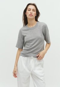 Tricou scurt din tricot, de culoare gri deschis, cu guler rotund și textură subtilă, purtat cu pantaloni albi largi, cu talie ajustabilă.