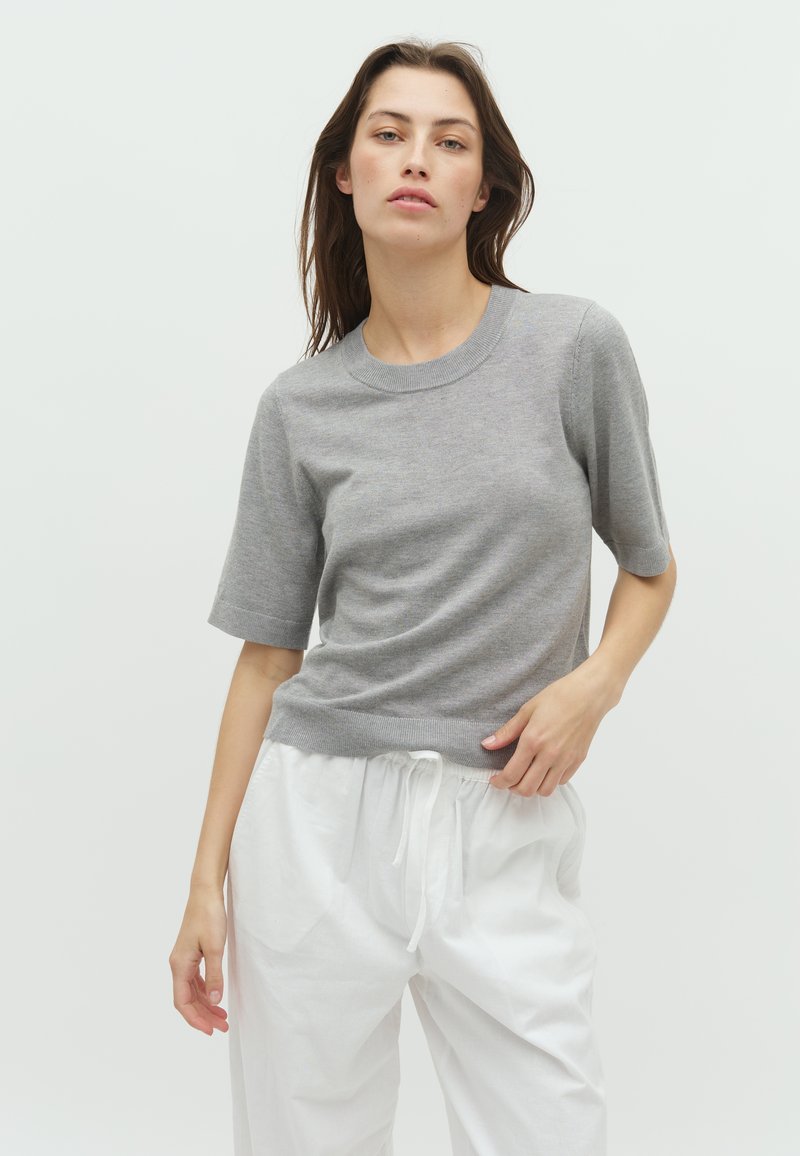 Tricou scurt din tricot, de culoare gri deschis, cu guler rotund și textură subtilă, purtat cu pantaloni albi largi, cu talie ajustabilă.