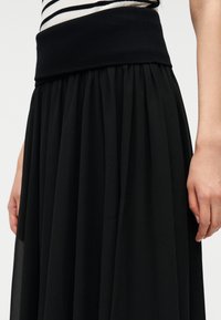 Μαύρη μακριά φούστα με υφασμάτινη, πλισέ σχεδίαση. Διαθέτει φαρδύ, ελαστικό ζωνάρι μέσης και ελαφρύ ύφασμα για αέρινη εμφάνιση.