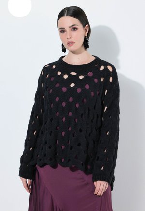 Maglione nero a maglia con un motivo a trama libera e maniche lunghe, indossato sopra un vestito viola scuro.
