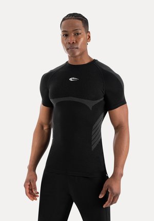 Sportlicher Mann mit geflochtenem Haar trägt ein schwarzes, kurzärmeliges Sportshirt mit dezenten strukturierten Mustern und einem kleinen weißen Logo auf der Brust.