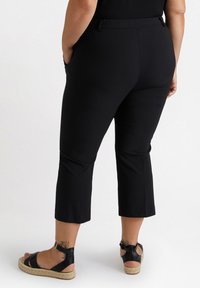Pantalons capri noirs avec une taille extensible, poches latérales et une texture lisse, associés à des sandales noires avec des brides autour de la cheville et des semelles tissées.