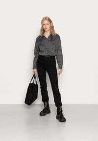 Gray, long-sleeve button-up shirt with two chest pockets, paired with black slim-fit jeans and chunky black boots. Carrying a black tote bag.