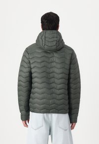 Padded, hooded jacket in olive green with a chevron quilted design. Features elastic cuffs and a relaxed fit. Soft, smooth texture.