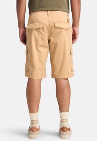 Pantaloni cargo beige con taglio dritto, due tasche laterali e due tasche posteriori. Realizzati in tessuto leggero con dettagli di cucitura visibili.