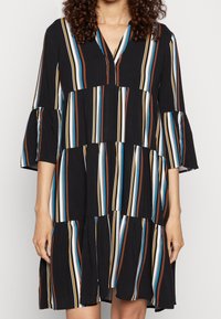 Černé šaty s vertikálními vícebarevnými pruhy v hnědé, modré a krémové barvě, s výstřihem do V a rozšířenými třičtvrtinovými rukávy.