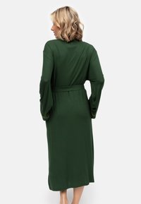 Un lungo e scuro abito verde con vita legata, caratterizzato da maniche a campana e dettagli gialli, realizzato in un morbido tessuto testurizzato. Vista posteriore.