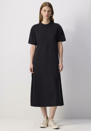 Abito midi in cotone nero con maniche corte, scollatura rotonda e vestibilità comoda. Abbinato a sneaker di colore chiaro per un look casual.