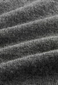 Pelēks adīts audums ar mīkstu, faktūrētu virsmu, kam ir ribota raksts un nedaudz nevienmērīgas krokas.