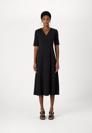 Black dress with vertical pinstripes, V-neck, short sleeves, flowing skirt, made of lightweight fabric. Paired with black sandals featuring buckles.