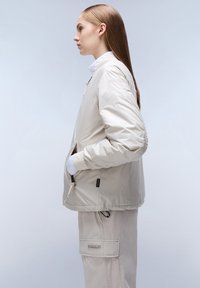 Beige, geïsoleerde jas met een ontspannen pasvorm, met ritszakken, ribgebreide manchetten en een trekkoord onderaan, gecombineerd met lichtgekleurde cargobroek.