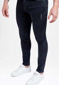 Kapeat, tummansiniset farkut, joissa on hieman haalistusta, vetoketjullinen etusuljenta ja viiden taskun malli, yhdistettynä valkoisiin tennareihin.