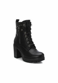 Botas negras hasta el tobillo con un alto tacón cuadrado, parte delantera con cordones, cremallera lateral, detalles de tachuelas y un acabado de cuero mate.