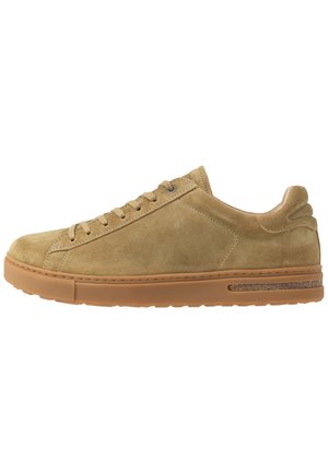 Beige suède low-top sneaker met bijpassende veters, een zool van gumrubber en subtiele stikseldetails aan de zijkant en hiel.