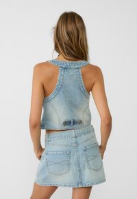 Jasnoniebieski krótki top z denimu z okrągłym kołnierzykiem i bez rękawów, zestawiony z pasującą spódnicą z jasnoniebieskiego denimu z tylnymi kieszeniami.
