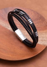 Zwarte leren armband met drie strengen, waarvan één gevlochten en twee glad, met zilveren accenten en een rechthoekige sluiting.