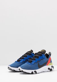 Blå sportskor med svarta snören och detaljer, med en vit sula och flerfärgade häldekorationer i röd och gul.