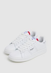 Sneaker bianchi realizzati in materiale sintetico liscio, con accenti rossi e blu, punta arrotondata, design con lacci e dettagli perforati sui lati.