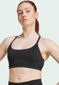 Sujeción deportiva negra sin costuras con tirantes anchos, escote redondeado y un diseño ajustado, fabricada en un material suave y elástico.