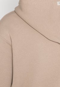 Felpa con cappuccio beige realizzata in morbido tessuto a costine. Presenta una vestibilità rilassata e un'etichetta minimale vicino al collo. Texture liscia senza motivi.