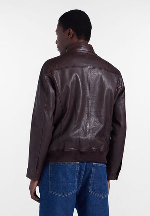 Braune Lederjacke mit geripptem Saum und Bündchen, mit glatter Textur und Stehkragen; von hinten mit blauen Jeans gezeigt.