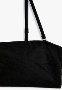 Sort tekstureret crop top med tynde stropper og justerbart udstyr. Stoffet har et subtilt mønster, der giver et krøllet udseende.